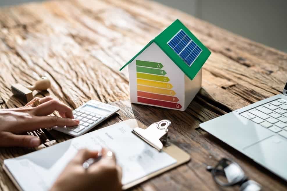 Personne calculant la performance énergétique avec maquette maison DPE et panneaux solaires sur bureau professionnel