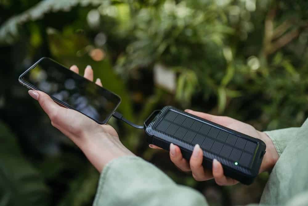 Personne utilisant un chargeur solaire portable pour recharger un smartphone en extérieur avec câble USB