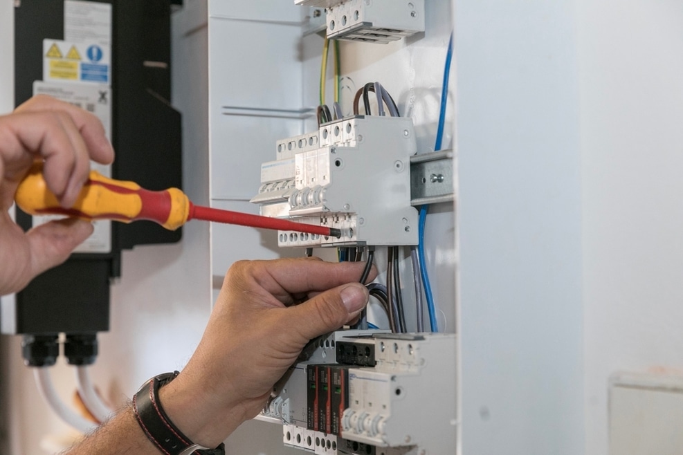 Électricien installant un disjoncteur pour panneau solaire dans tableau électrique avec tournevis isolé