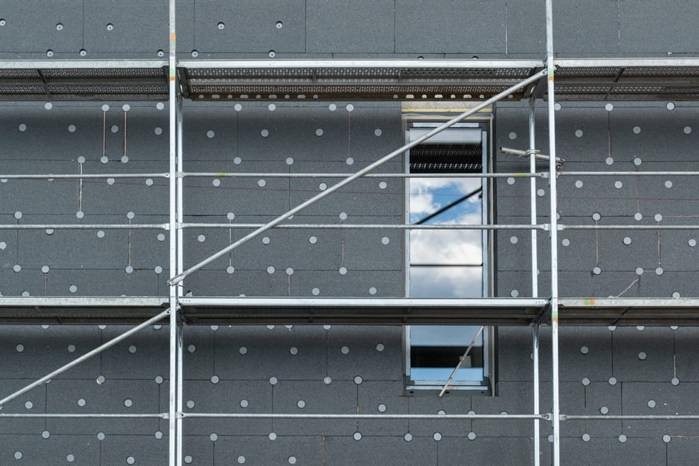 Façade de bâtiment avec isolation thermique extérieure grise fixée sur échafaudage durant travaux de rénovation énergétique