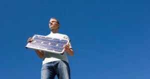 Homme souriant tenant petit panneau solaire photovoltaïque sous ciel bleu dégagé pour production optimale d'énergie