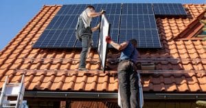 Techniciens professionnels installant des panneaux solaires photovoltaïques sur toit en tuiles orange avec échelle