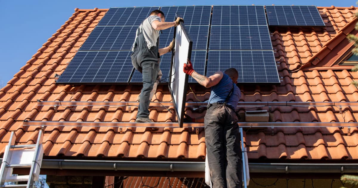 Techniciens professionnels installant des panneaux solaires photovoltaïques sur toit en tuiles orange avec échelle