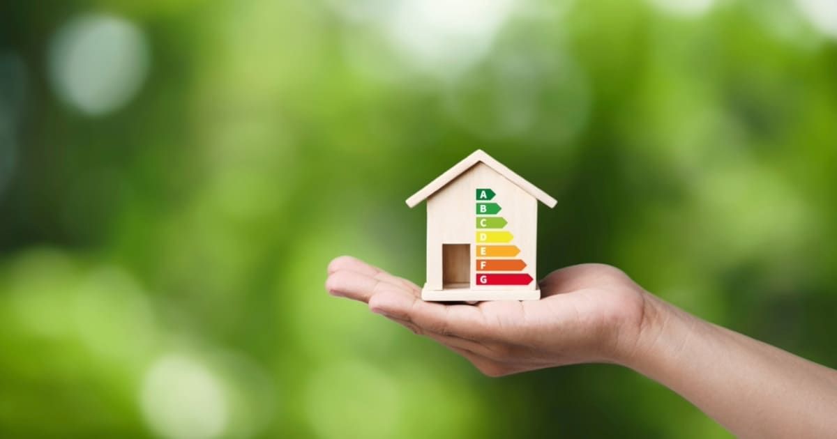 Main tenant petite maquette de maison avec étiquette DPE colorée représentant diagnostic de performance énergétique
