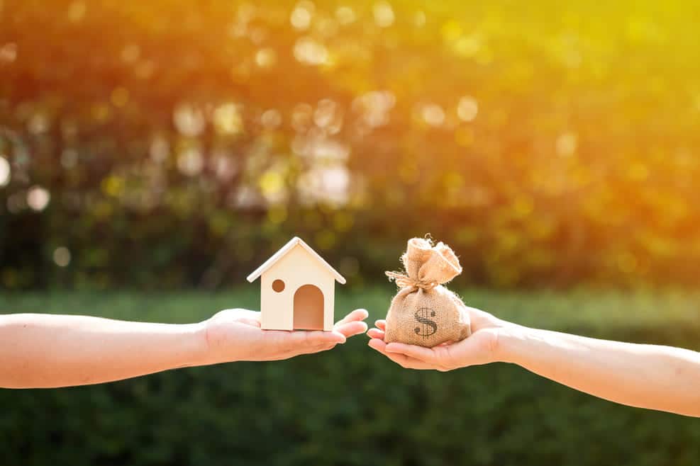 Deux mains tenant maquette de maison et sac d'argent symbolisant le financement et investissement en rénovation énergétique