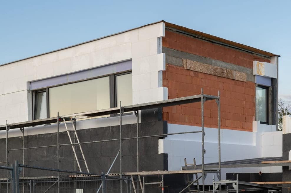 Maison contemporaine en construction montrant isolation thermique extérieure ITE avec façade mixte briques et enduit blanc