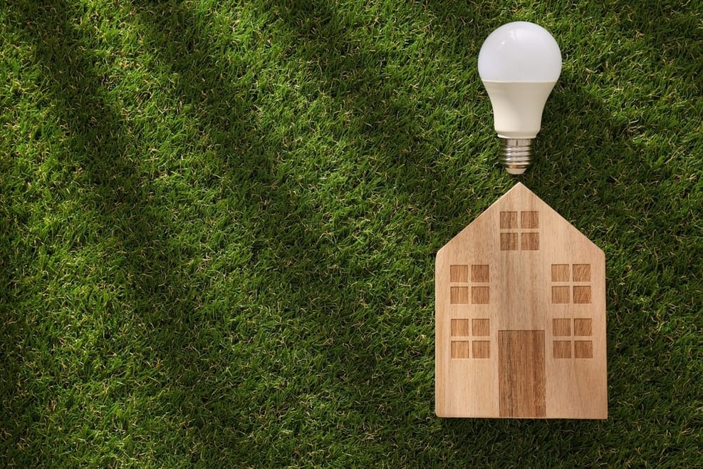 Maquette de maison en bois avec ampoule LED allumée symbolisant production énergie solaire et efficacité énergétique