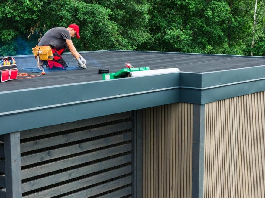 Ouvrier appliquant membrane d'étanchéité EPDM sur toit plat en préparation pour installation de panneaux solaires