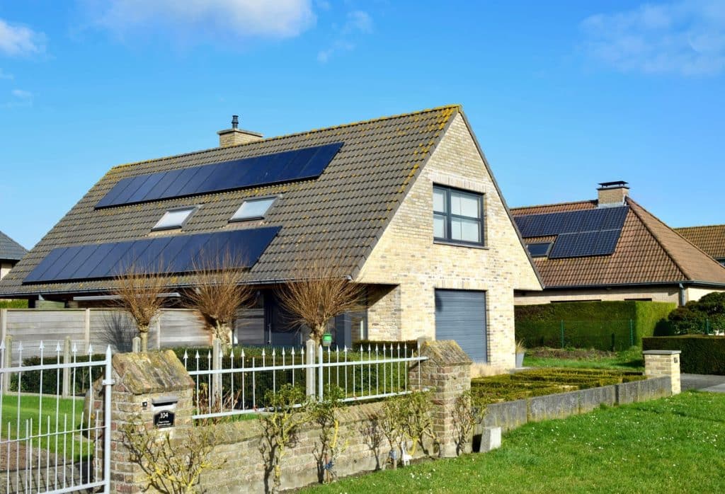Maison individuelle équipée de panneaux solaires photovoltaïques 9 kW sur toiture avec fenêtres de toit et jardin paysagé