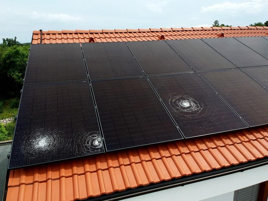 Panneaux solaires noirs installés sur toiture en tuiles orange avec traces circulaires d'impacts et risques de fissures