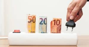 Main débranchant une prise électrique avec billets d'euros illustrant les économies d'énergie en supprimant la consommation fantôme