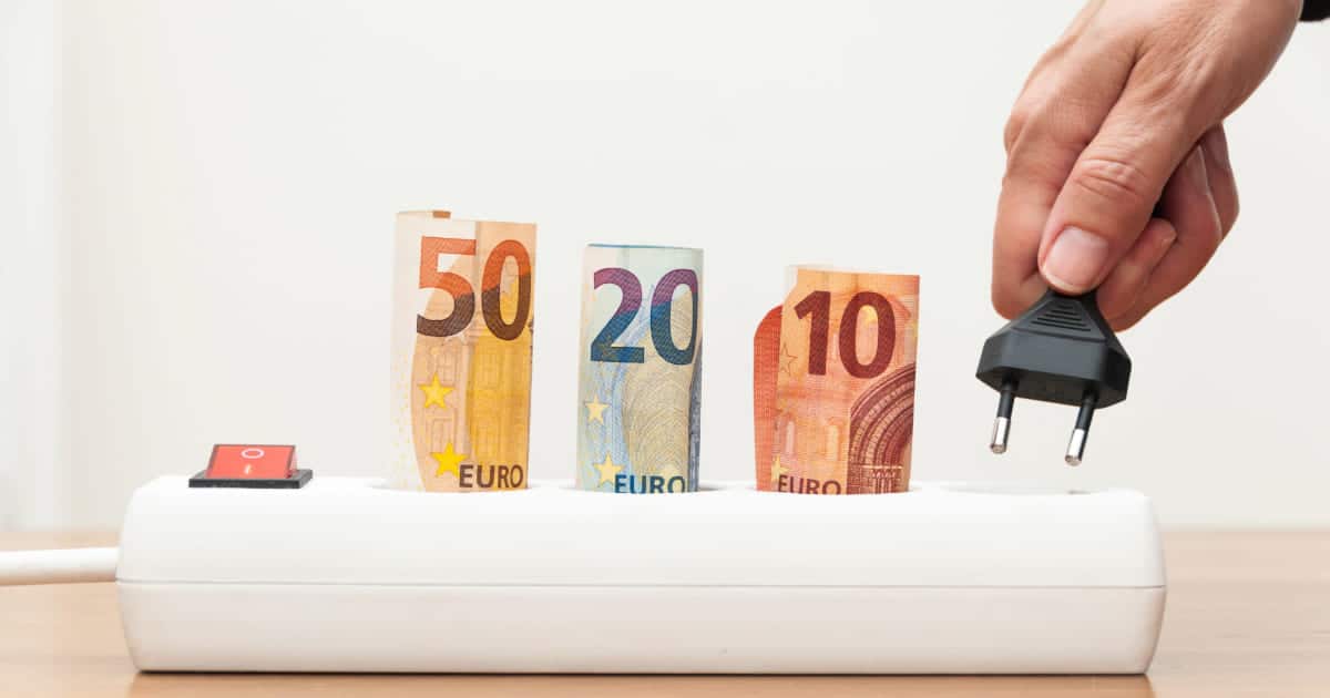Main débranchant une prise électrique avec billets d'euros illustrant les économies d'énergie en supprimant la consommation fantôme
