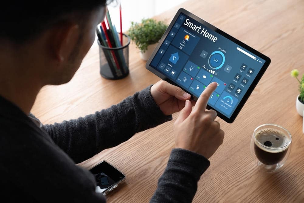Personne utilisant tablette avec application Smart Home Somfy pour contrôler température et éclairage maison connectée