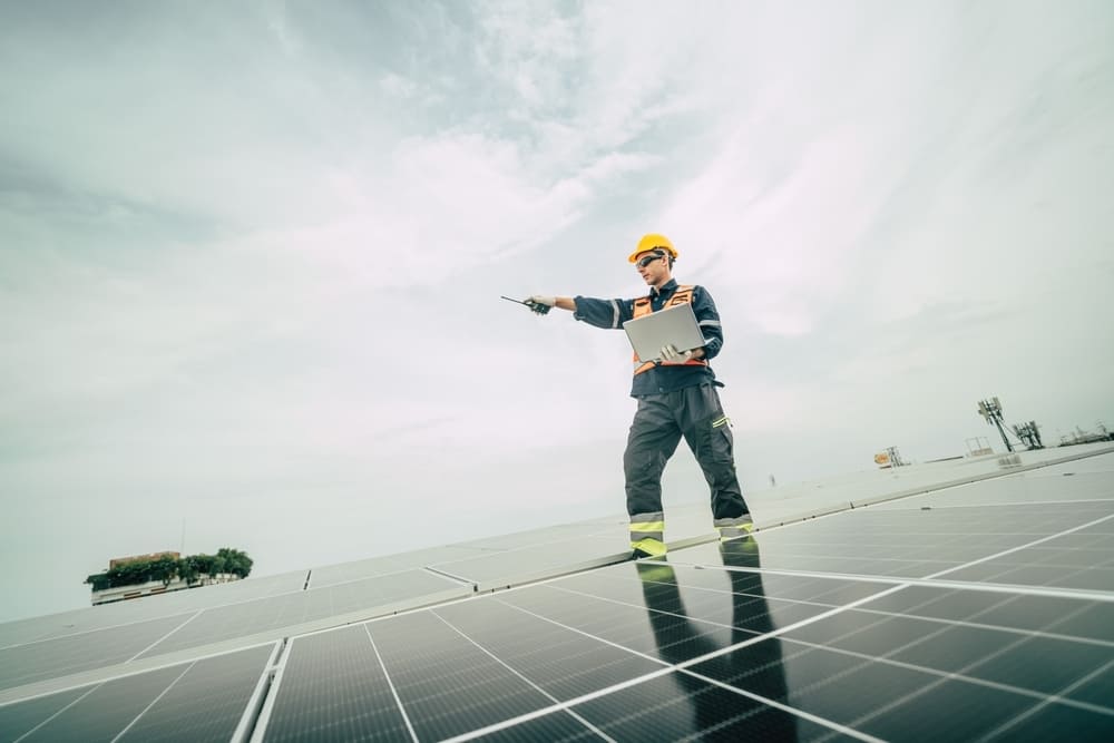 Technicien avec casque jaune inspectant installation panneaux solaires sous ciel nuageux affectant production photovoltaïque