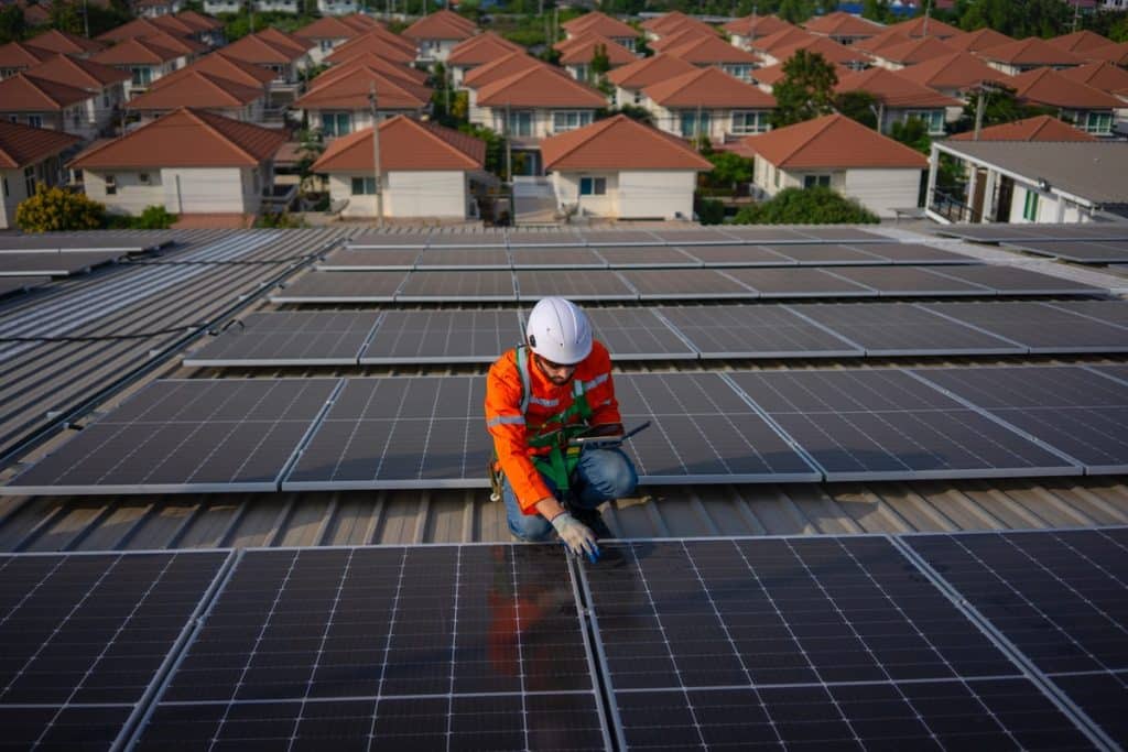 Technicien professionnel installant une centrale photovoltaïque 9 kW sur toiture plate avec quartier résidentiel en arrière-plan