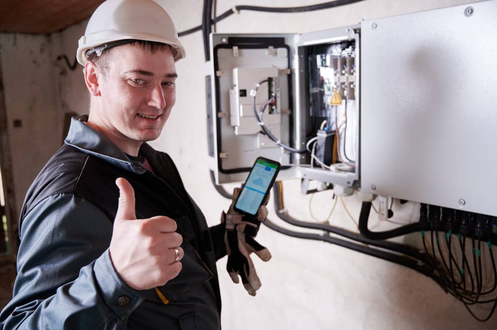 Technicien installateur configurant un régulateur MPPT et onduleur solaire avec application smartphone de monitoring