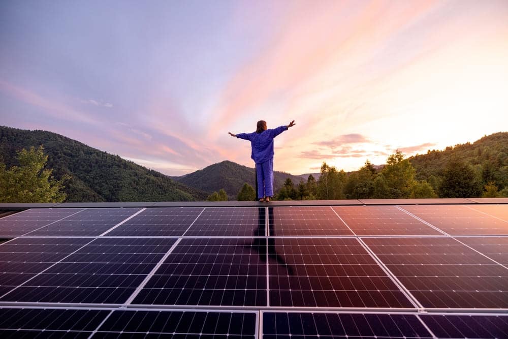 Personne contemplant le coucher de soleil devant son installation de panneaux solaires symbolisant l'autonomie énergétique