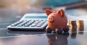 Tirelire et calculatrice posées sur un panneau solaire avec des pièces de monnaie, symbolisant les économies et la rentabilité d'une installation photovoltaïque