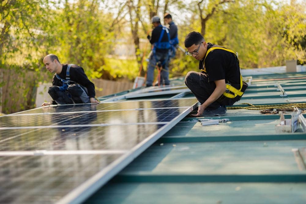 Équipe d'installateurs munis de harnais de sécurité posant des panneaux solaires photovoltaïques sur une toiture