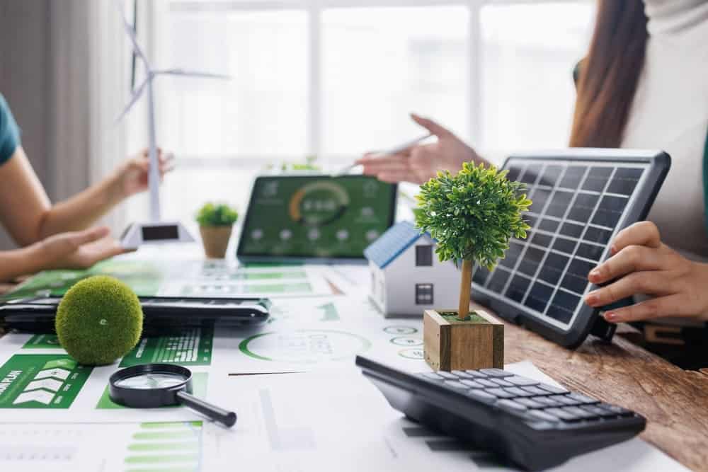 Équipe analysant un projet d'énergie solaire avec panneau photovoltaïque, maquette de maison et documents sur la transition écologique