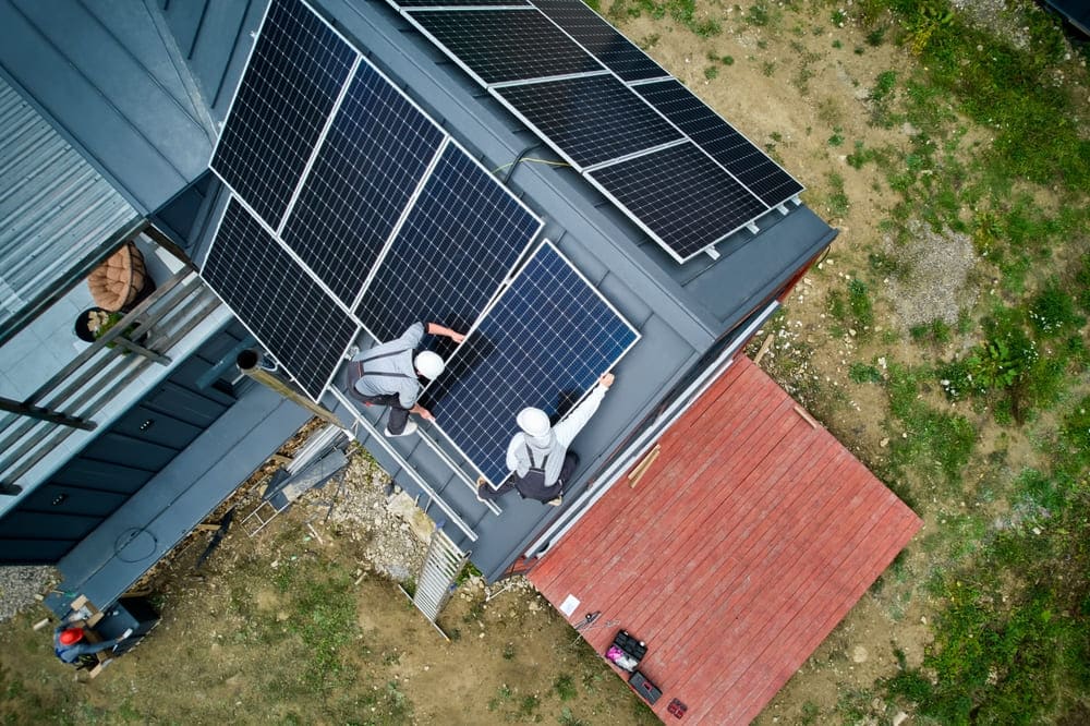 Vue aérienne de deux installateurs portant des casques de sécurité pour poser des panneaux solaires sur un toit