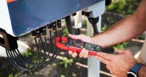 Technicien mesurant le courant électrique sur les connecteurs d'un onduleur solaire avec une pince ampèremétrique