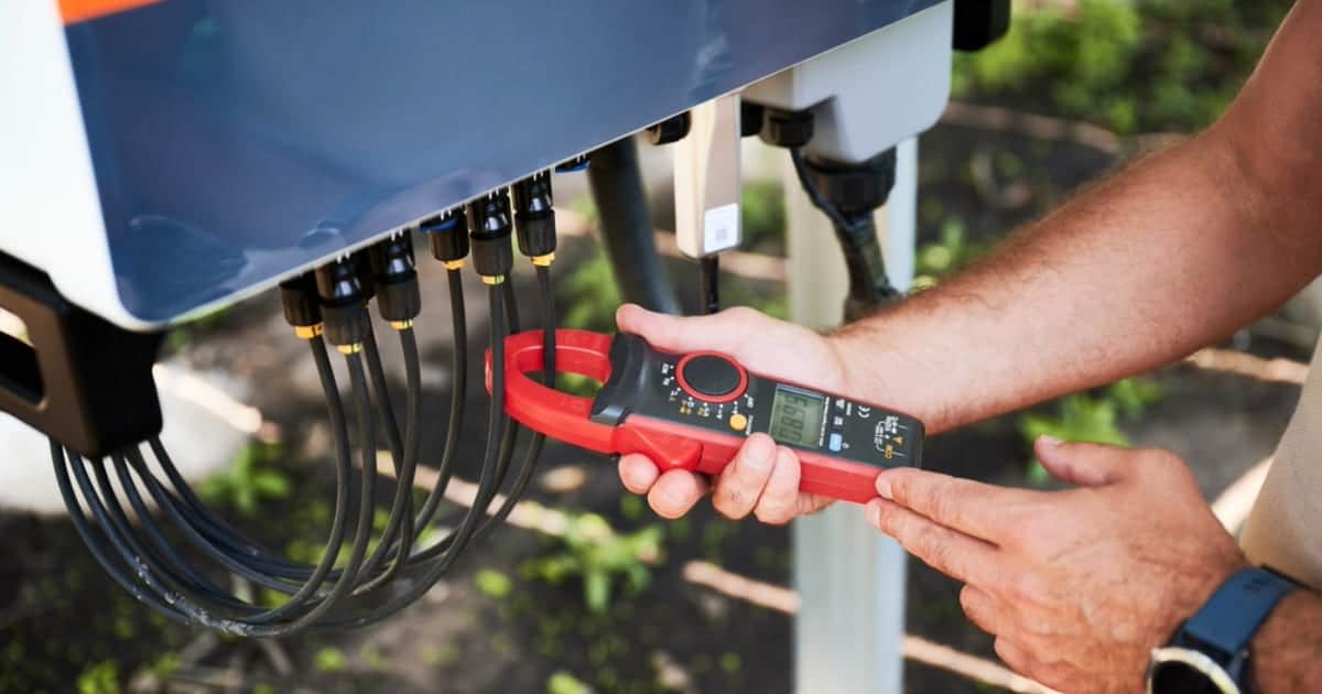 Technicien mesurant le courant électrique sur les connecteurs d'un onduleur solaire avec une pince ampèremétrique