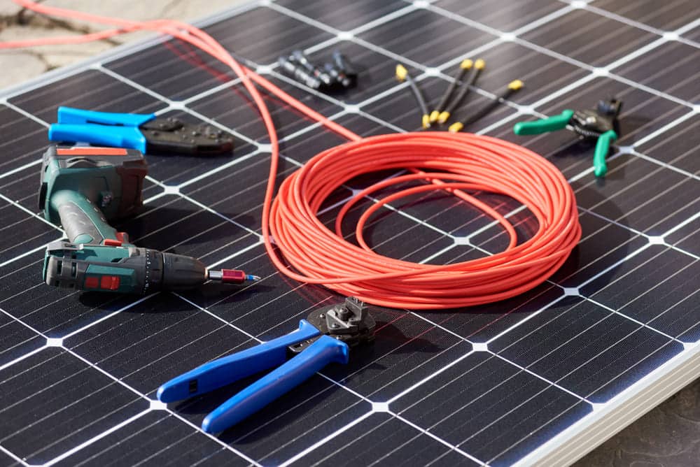 Outils nécessaires à l'installation d'un micro-onduleur : perceuse, pinces, câbles et connecteurs MC4 sur panneau solaire
