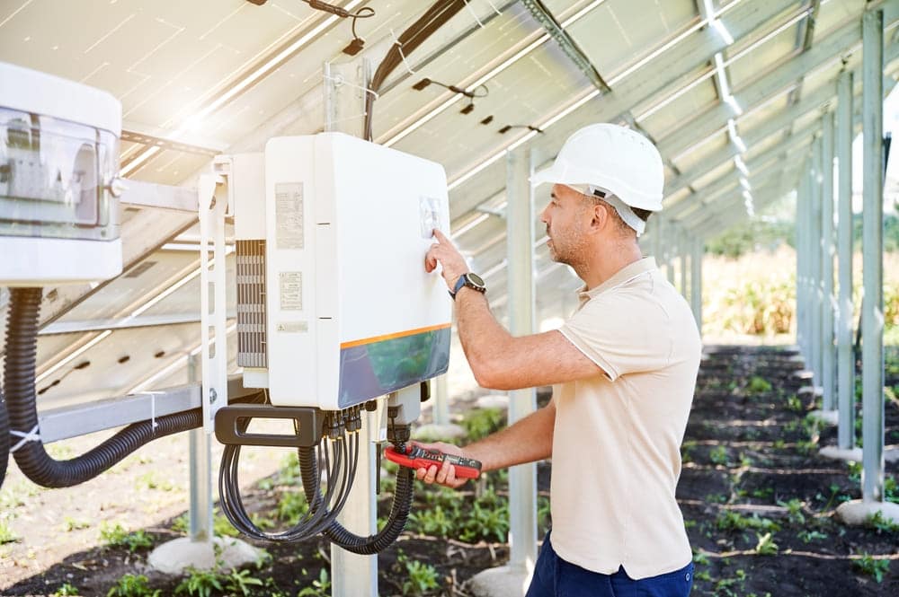 Technicien avec casque de sécurité intervenant sur un onduleur solaire sous une installation photovoltaïque