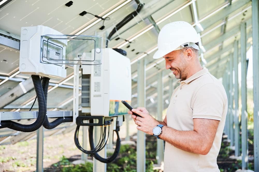 Technicien contrôlant un onduleur solaire avec application smartphone pour le suivi de production photovoltaïque