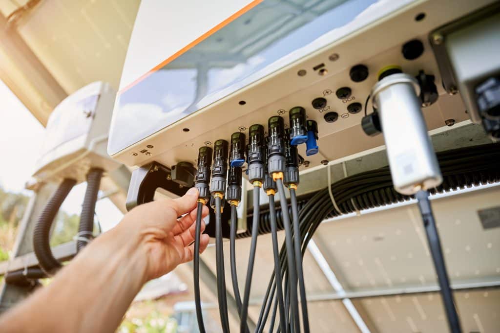 Installateur branchant des connecteurs MC4 sur un onduleur solaire pour raccorder les panneaux photovoltaïques