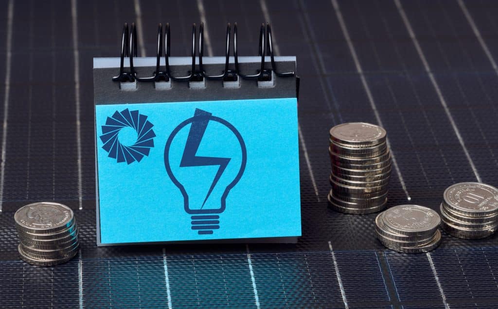  Icône d'ampoule électrique et pièces de monnaie posées sur un panneau solaire illustrant le dimensionnement économique d'une batterie solaire