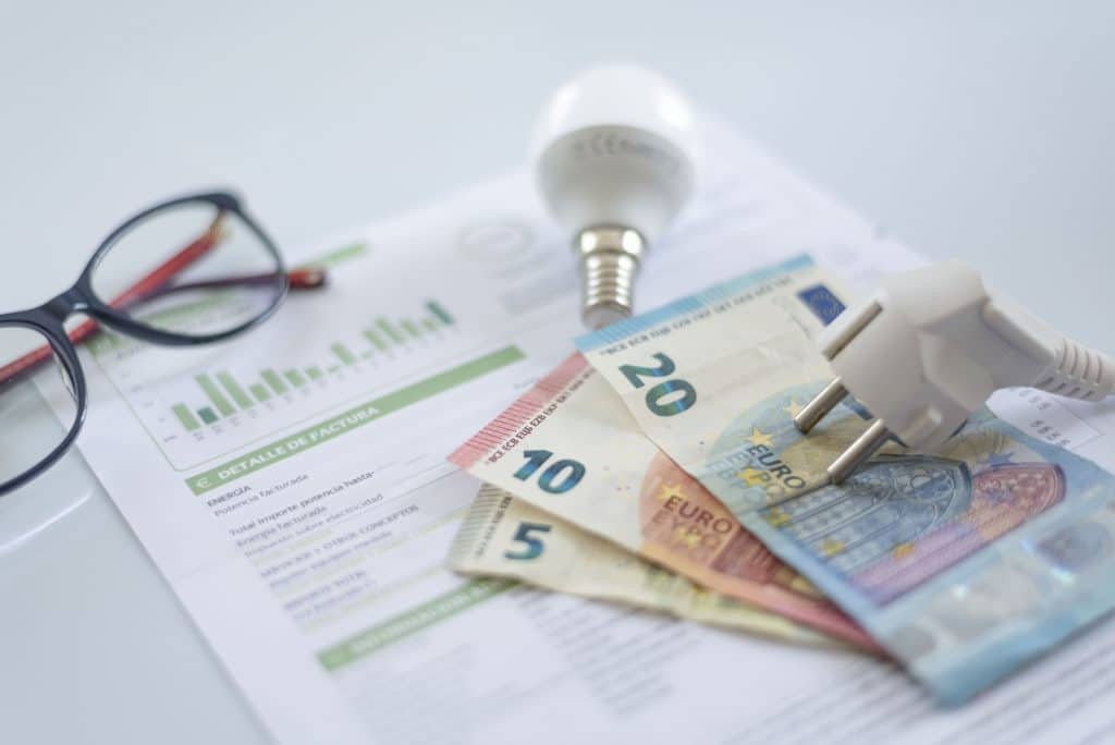 Facture d'électricité avec billets en euros, ampoule et prise électrique illustrant les économies réalisées grâce à une batterie solaire