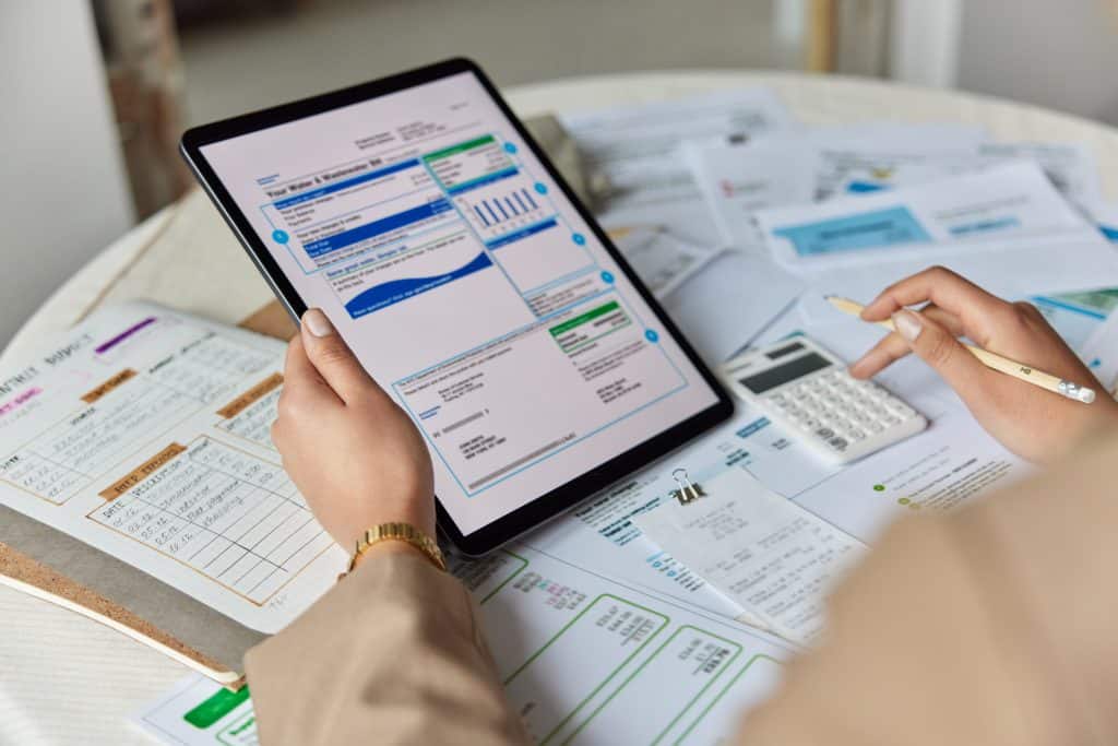 analyse-facture-electricite-performance-panneau-solaire Personne analysant ses factures d'électricité sur tablette avec calculatrice pour vérifier la rentabilité de son installation solaire