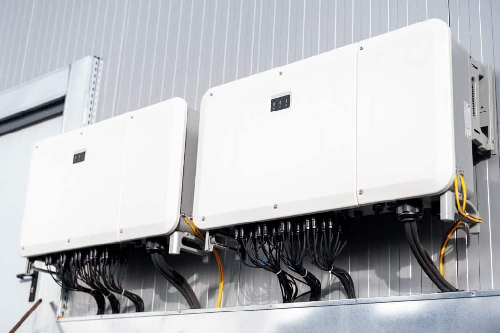 Trois onduleurs solaires blancs installés au mur avec câblage illustrant une installation photovoltaïque type Fronius ou SMA
