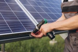 Technicien fixant un panneau solaire sur sa structure de support avec une visseuse pour une installation plug and play