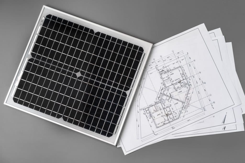Panneau solaire posé sur des plans d'architecte illustrant la phase de conception et de dimensionnement d'une installation photovoltaïque