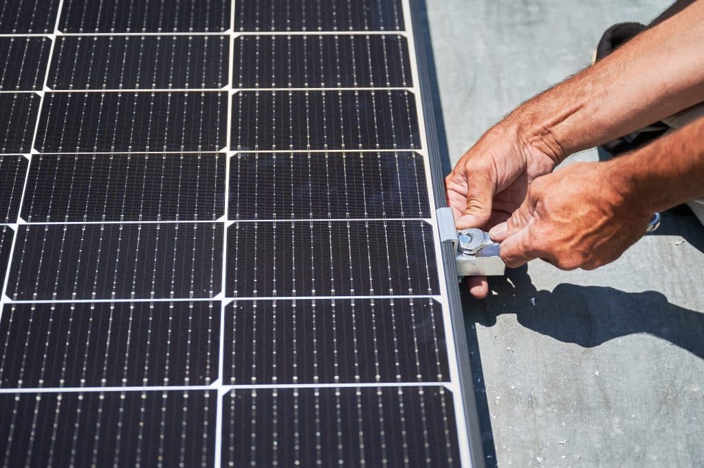 Gros plan sur les mains d'un installateur serrant une bride de fixation sur le cadre d'un panneau solaire plug and play