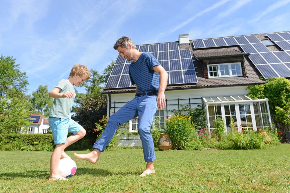 Père et fils jouant devant une maison équipée de panneaux solaires